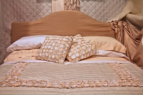 Made bed with richly decorated pillows and ornate bedspread. Beige themed bedroom with double bed.